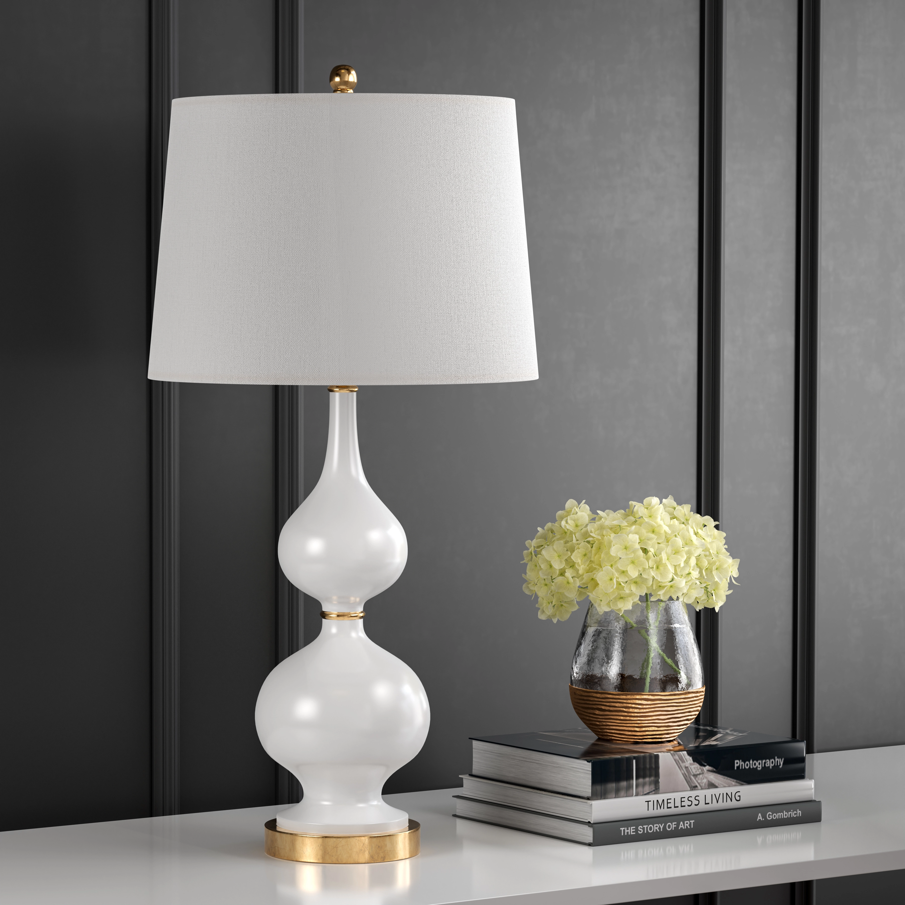 White gourd-shaped ceramic table lamp with a gold base and linen shade next to hydrangeas