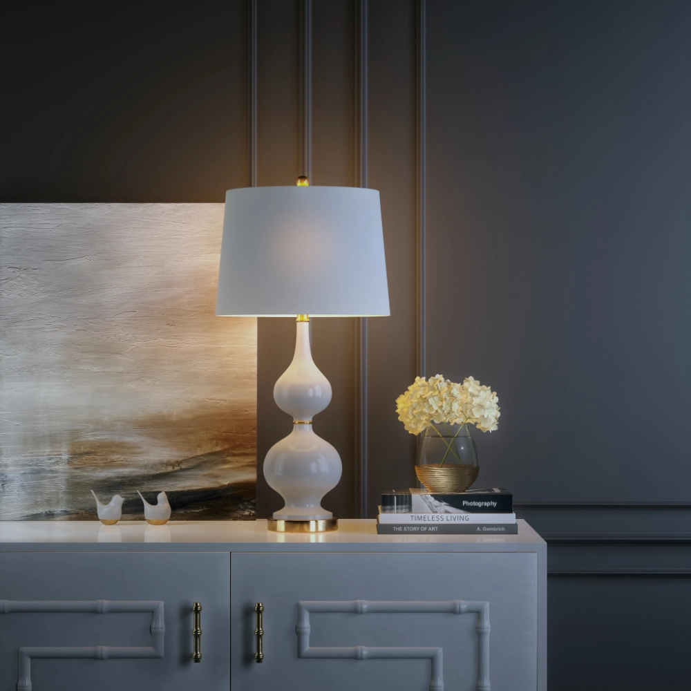 White gourd-shaped table lamp switched on, on a sideboard against a dark panelled wall